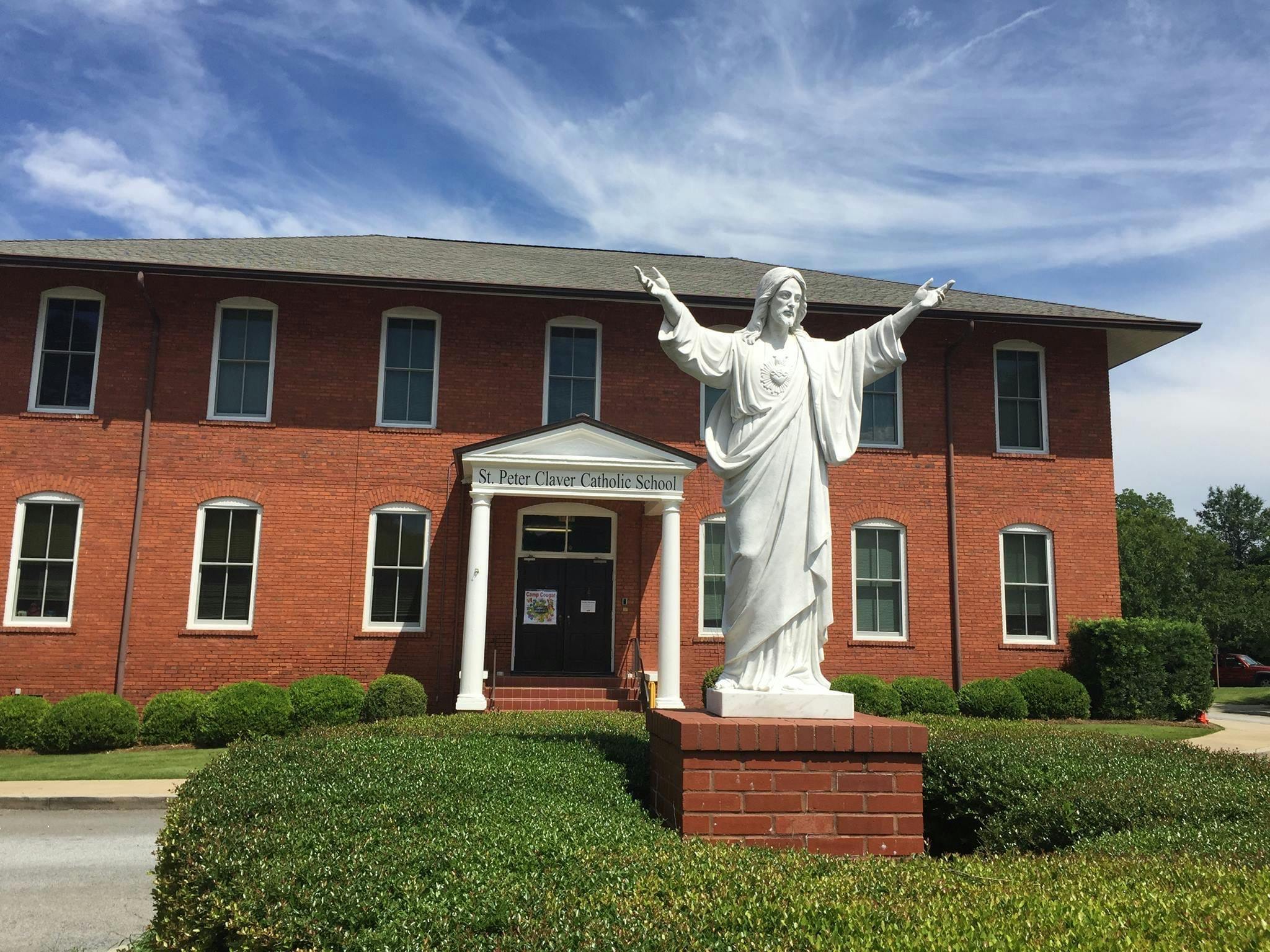 White statue of a person with arms outstretched in front of a brick building