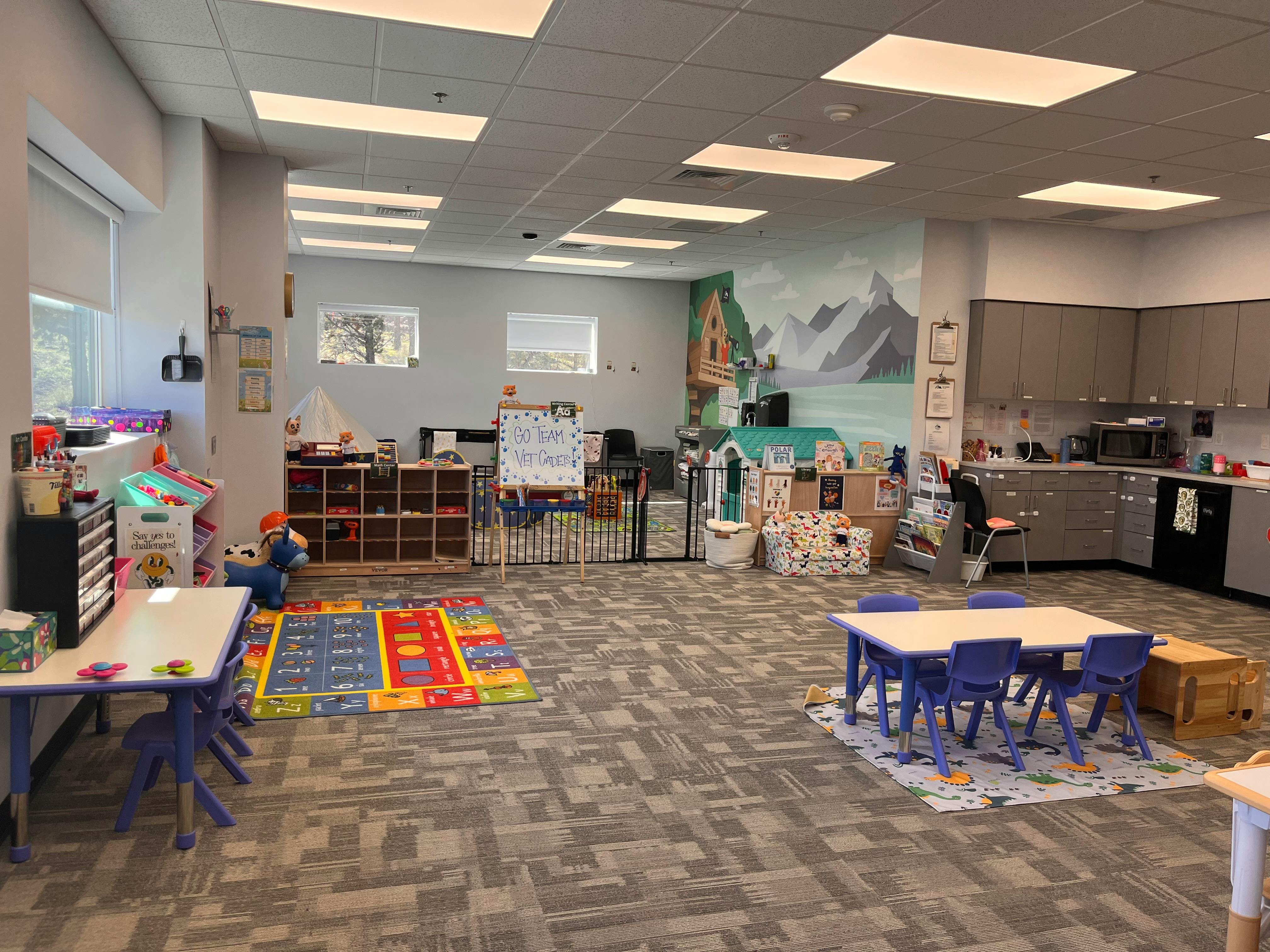 Playroom with small tables and chairs, play kitchen, and colorful rug