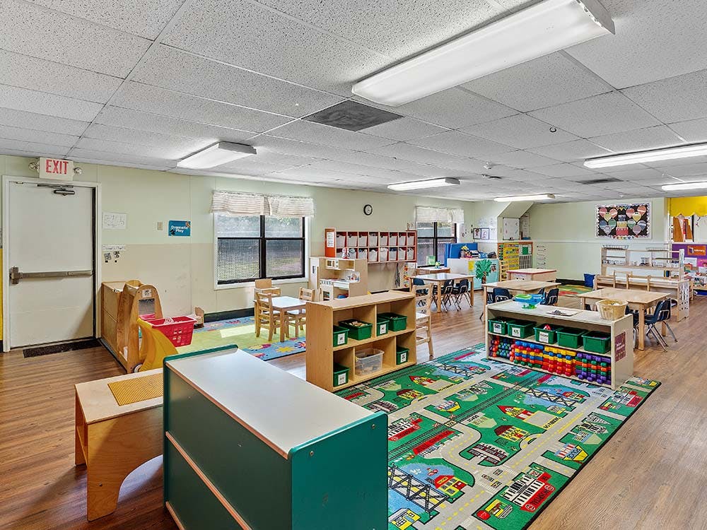 A classroom with small tables and chairs, storage units, and a colorful rug
