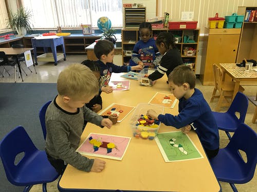 Children playing with colorful shapes at a table in a classroom