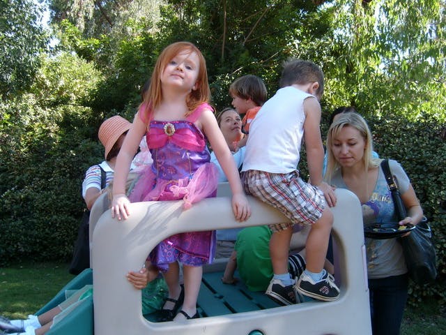 Child in a dress on a playground structure with other children and adults