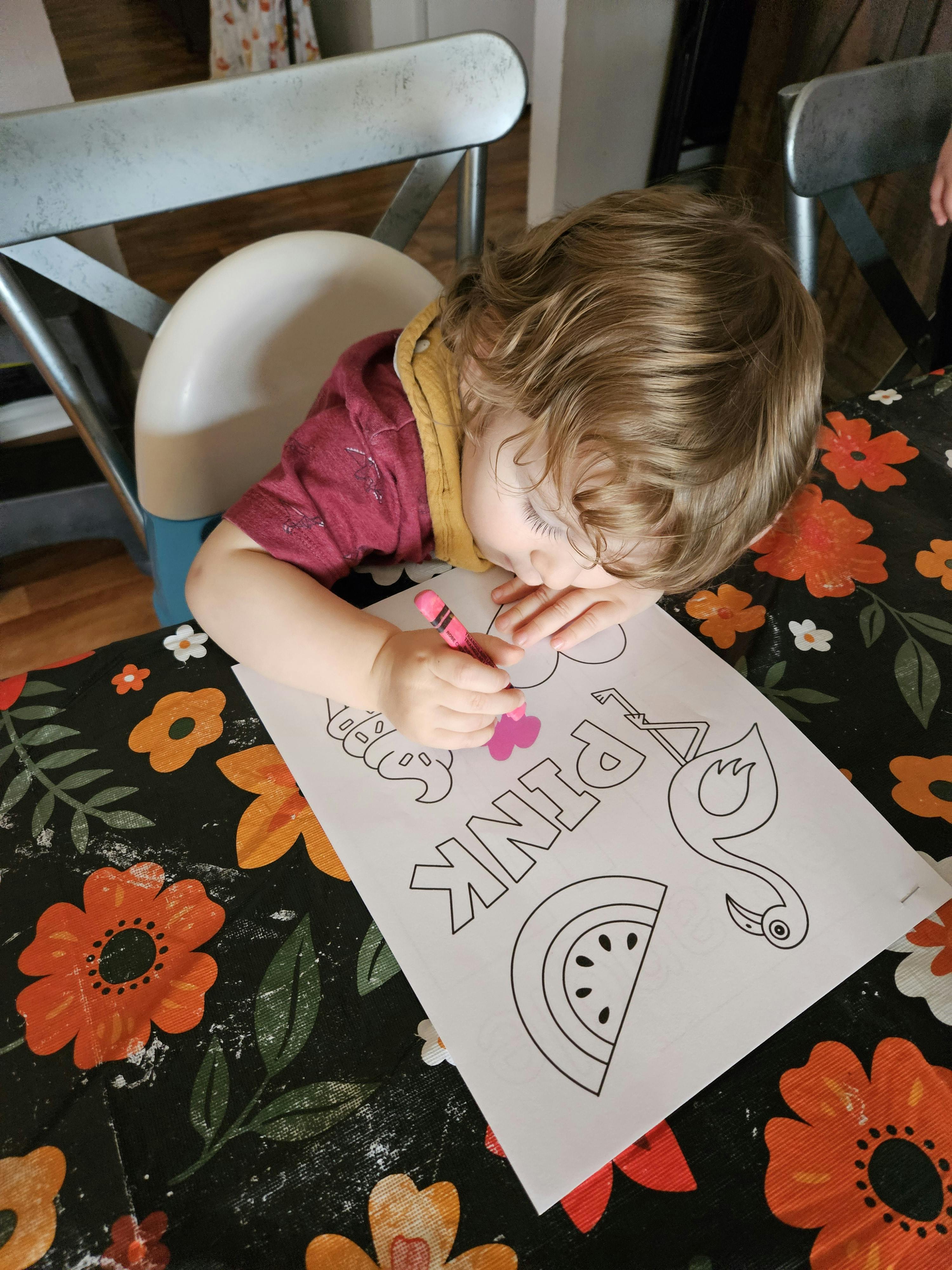 Child coloring a flamingo and watermelon worksheet with a pink crayon