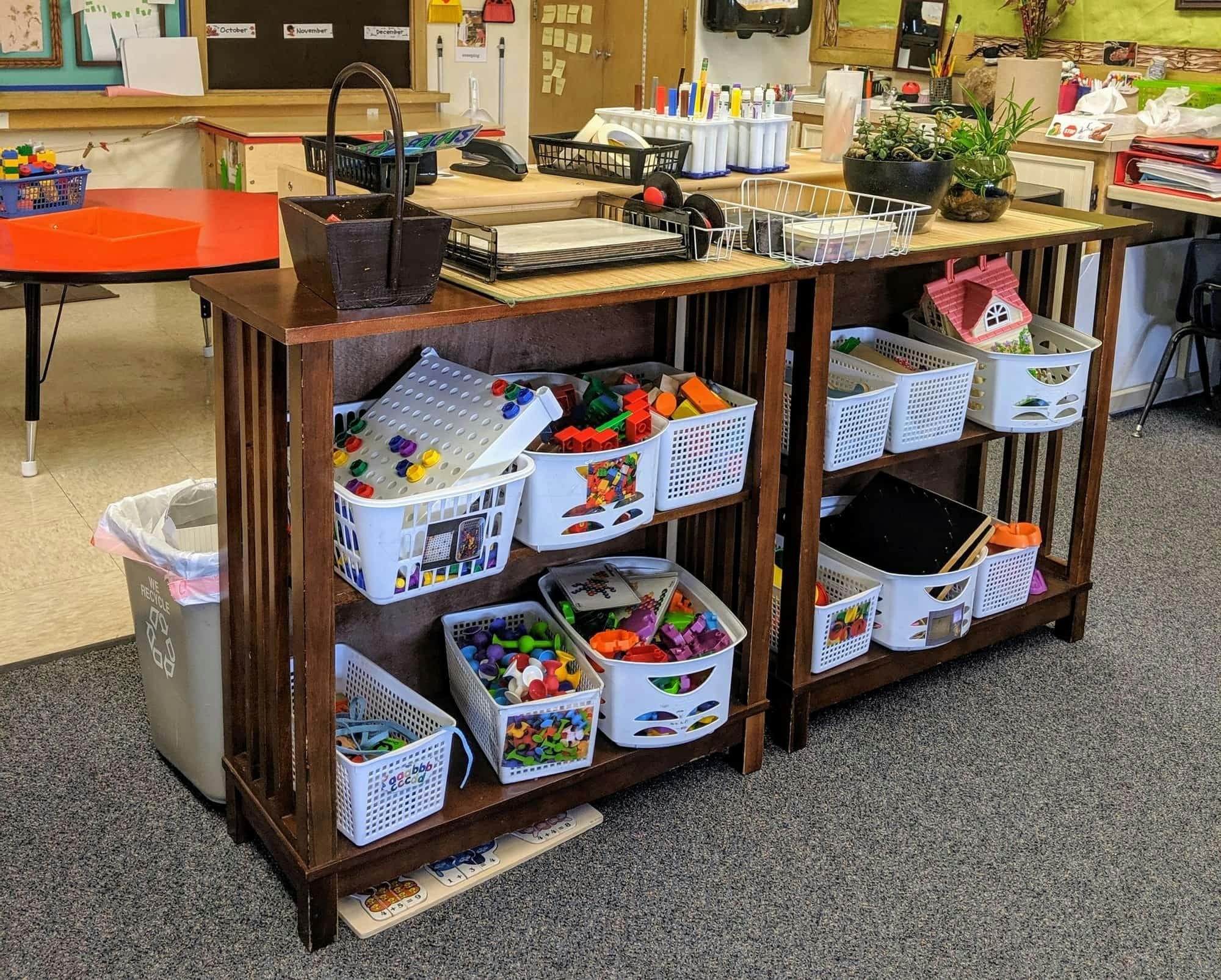 Wooden shelving unit with white baskets filled with toys in a classroom