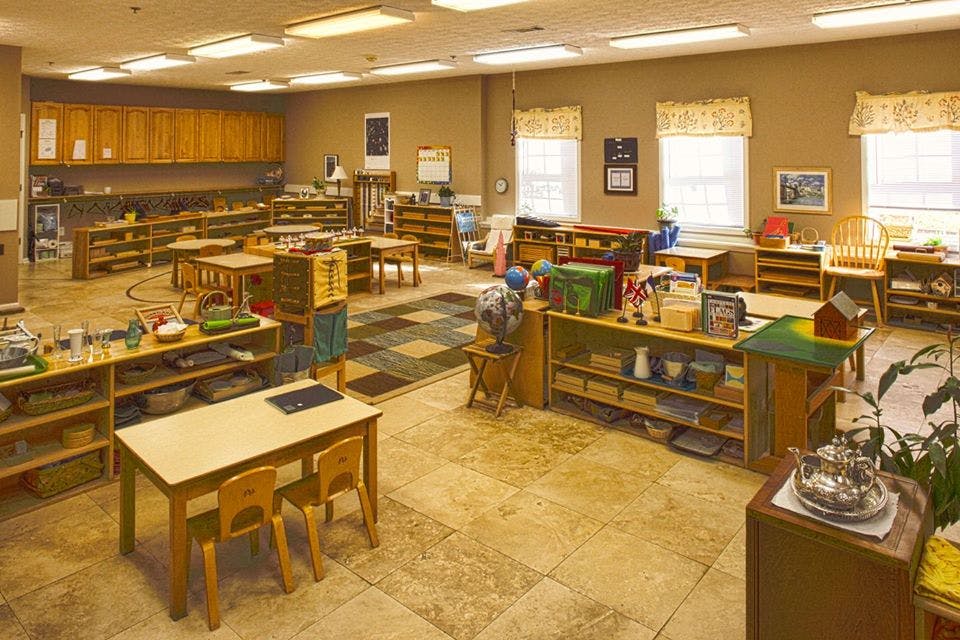 Classroom with small tables and chairs, shelves with learning materials