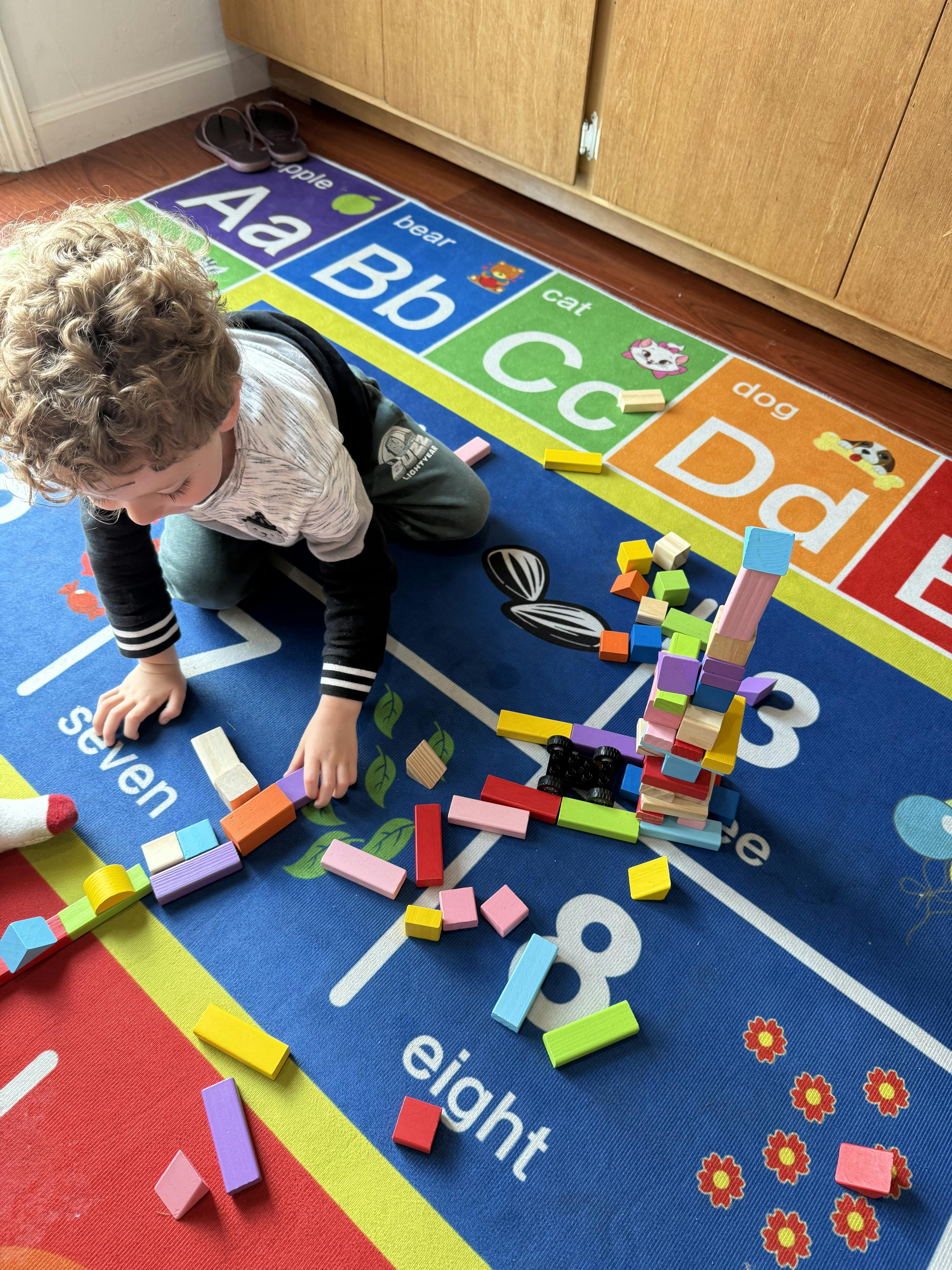 Child playing with colorful building blocks on an alphabet rug
