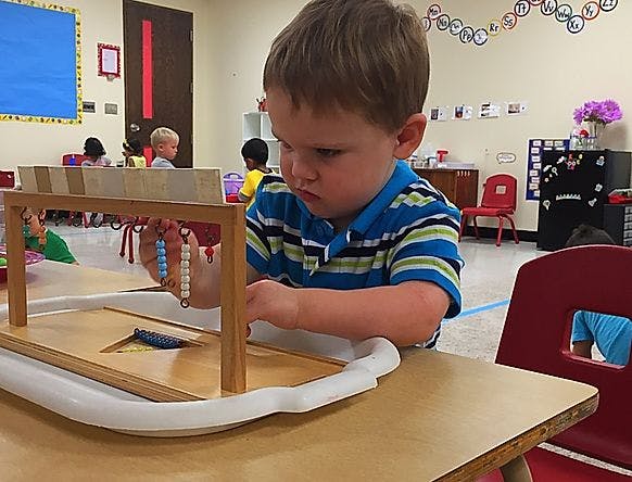 Child playing with an abacus-like toy in a classroom