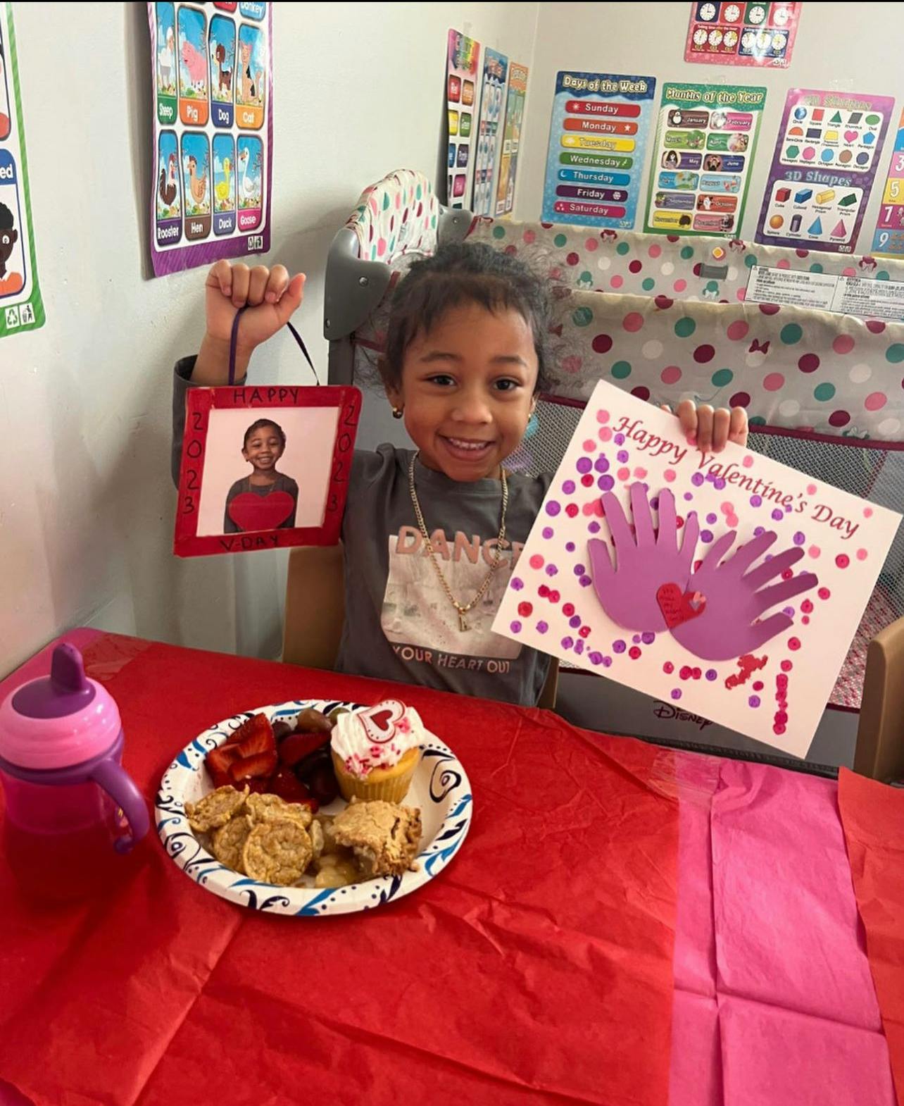 Child holding a framed photo and a handmade card that says "Happy Valentine's Day"