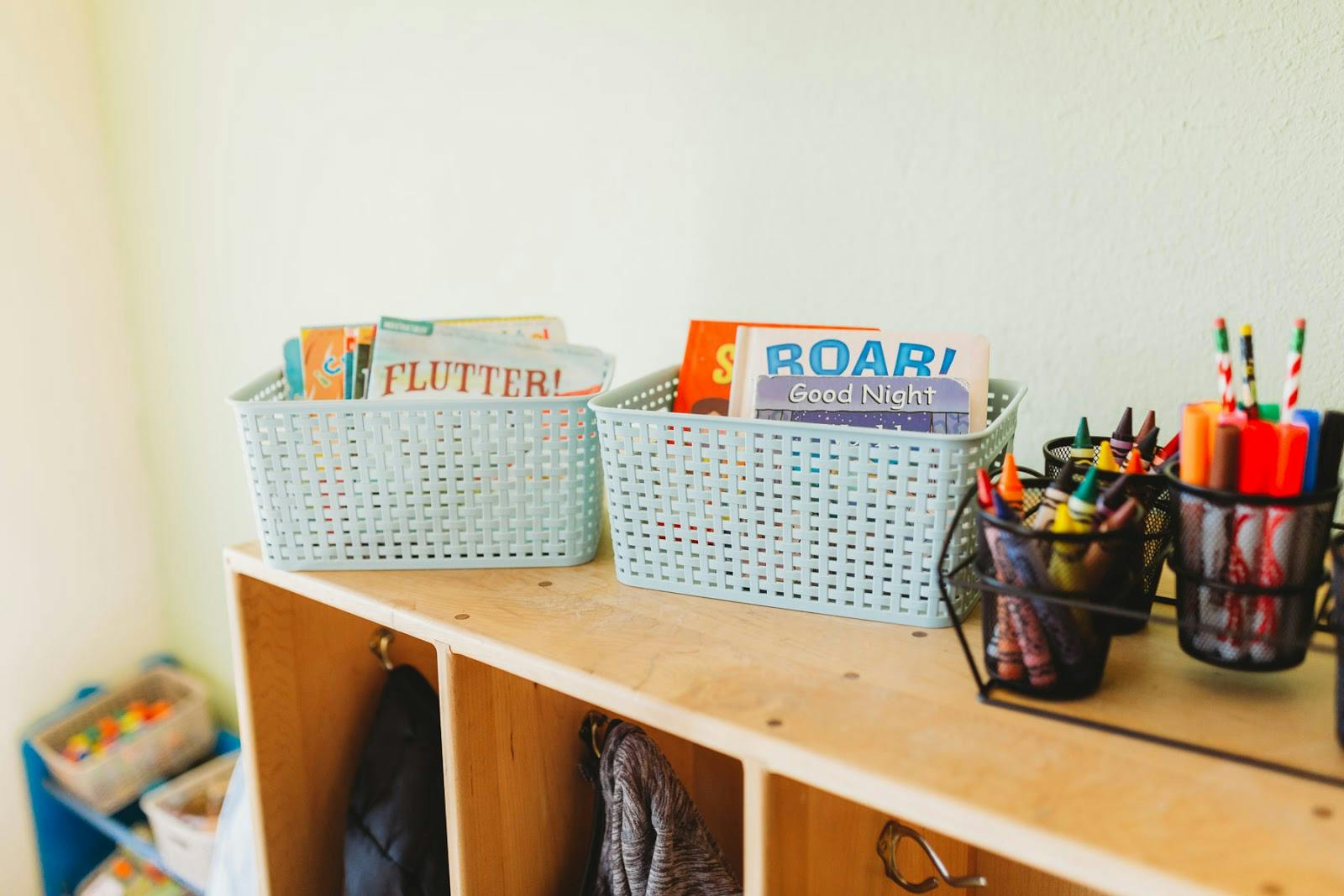 Baskets of books and containers of art supplies on a wooden shelf