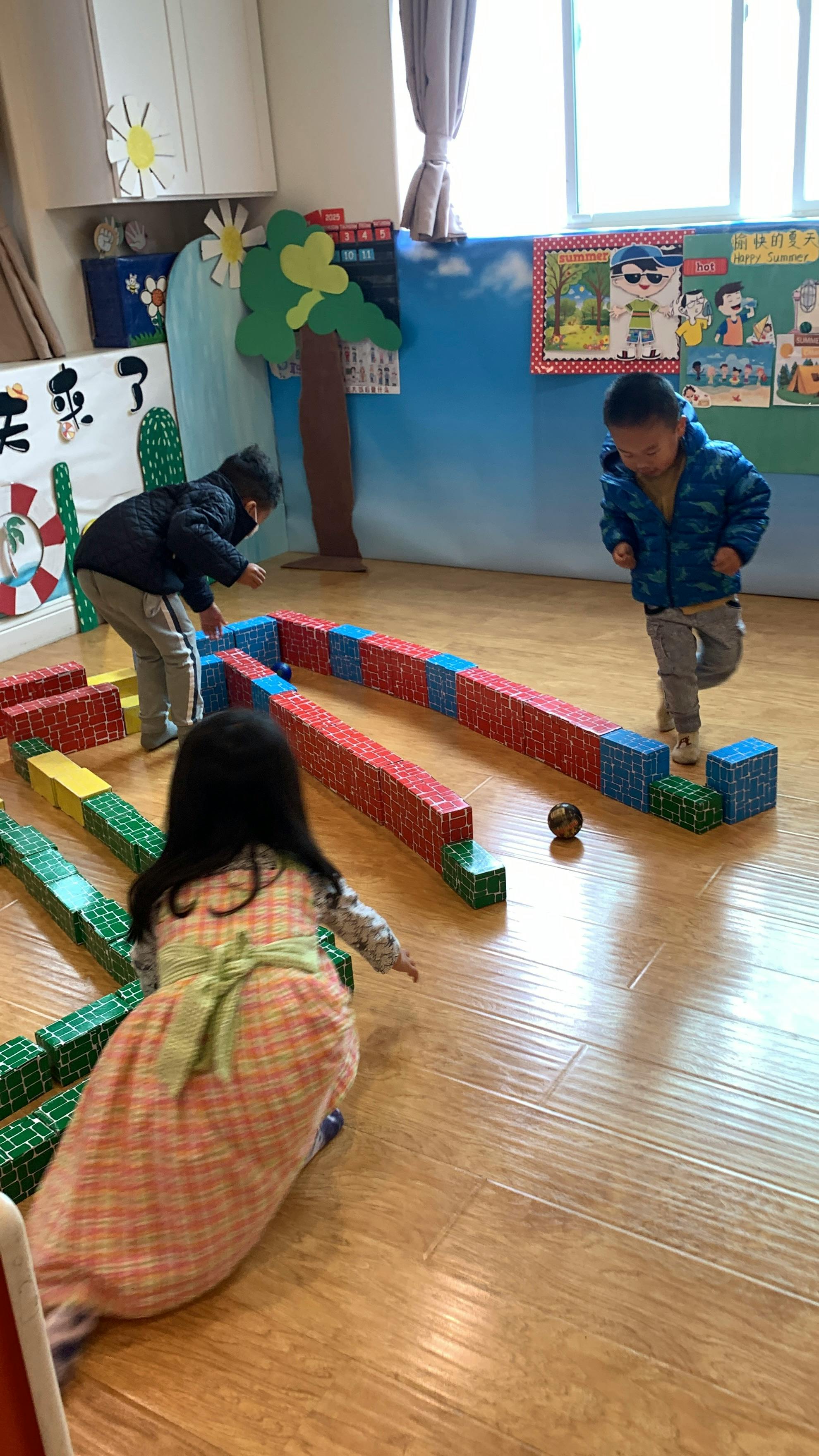 Three children playing with blocks and a ball on a wooden floor