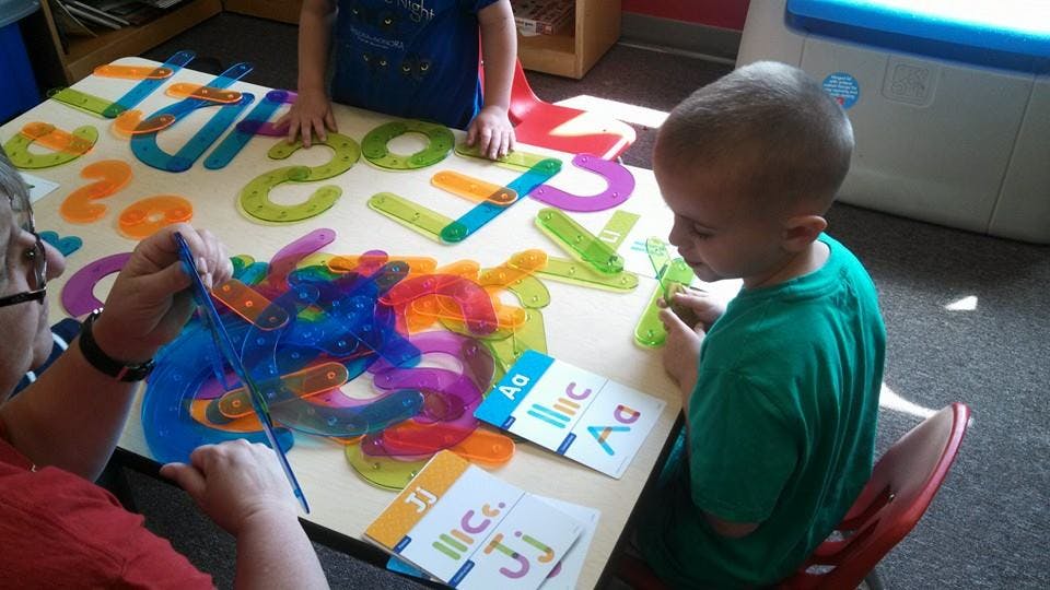Person and child playing with colorful letter toys at a table