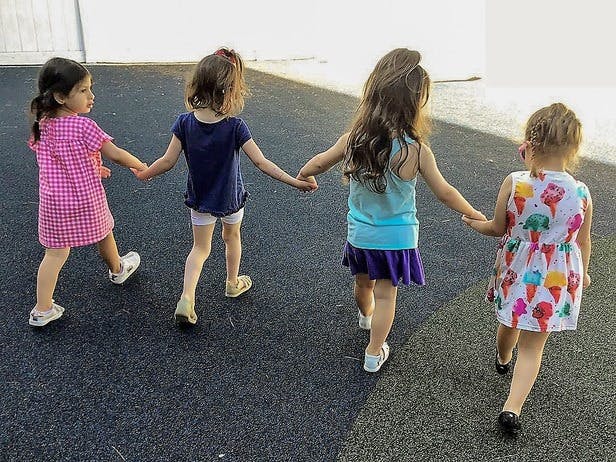Four children holding hands and walking away from behind