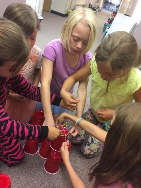 Children building a structure with red cups and rubber bands