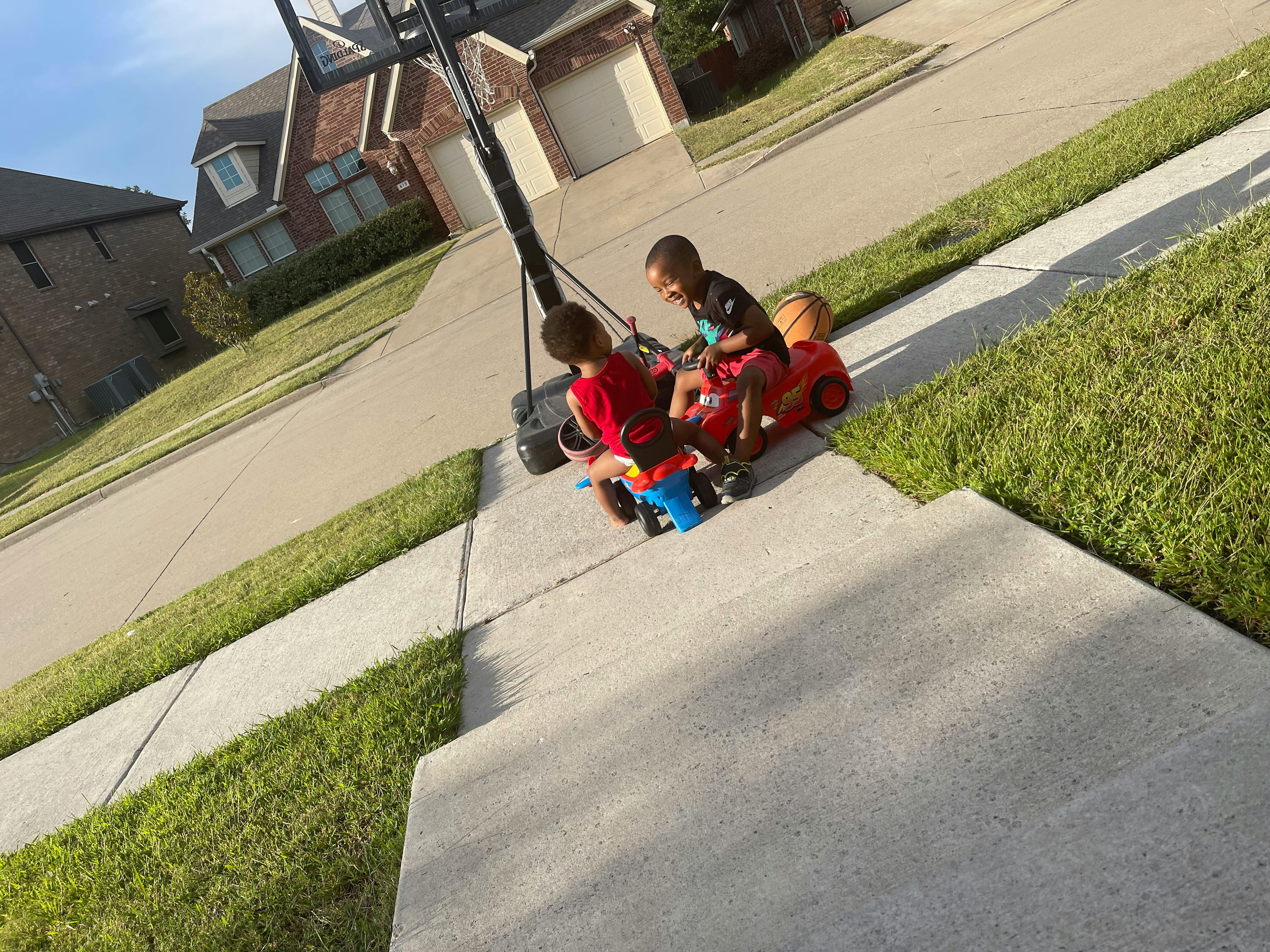 Two children on ride-on toys on a sidewalk