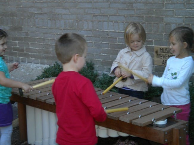Three children playing a large wooden xylophone outdoors