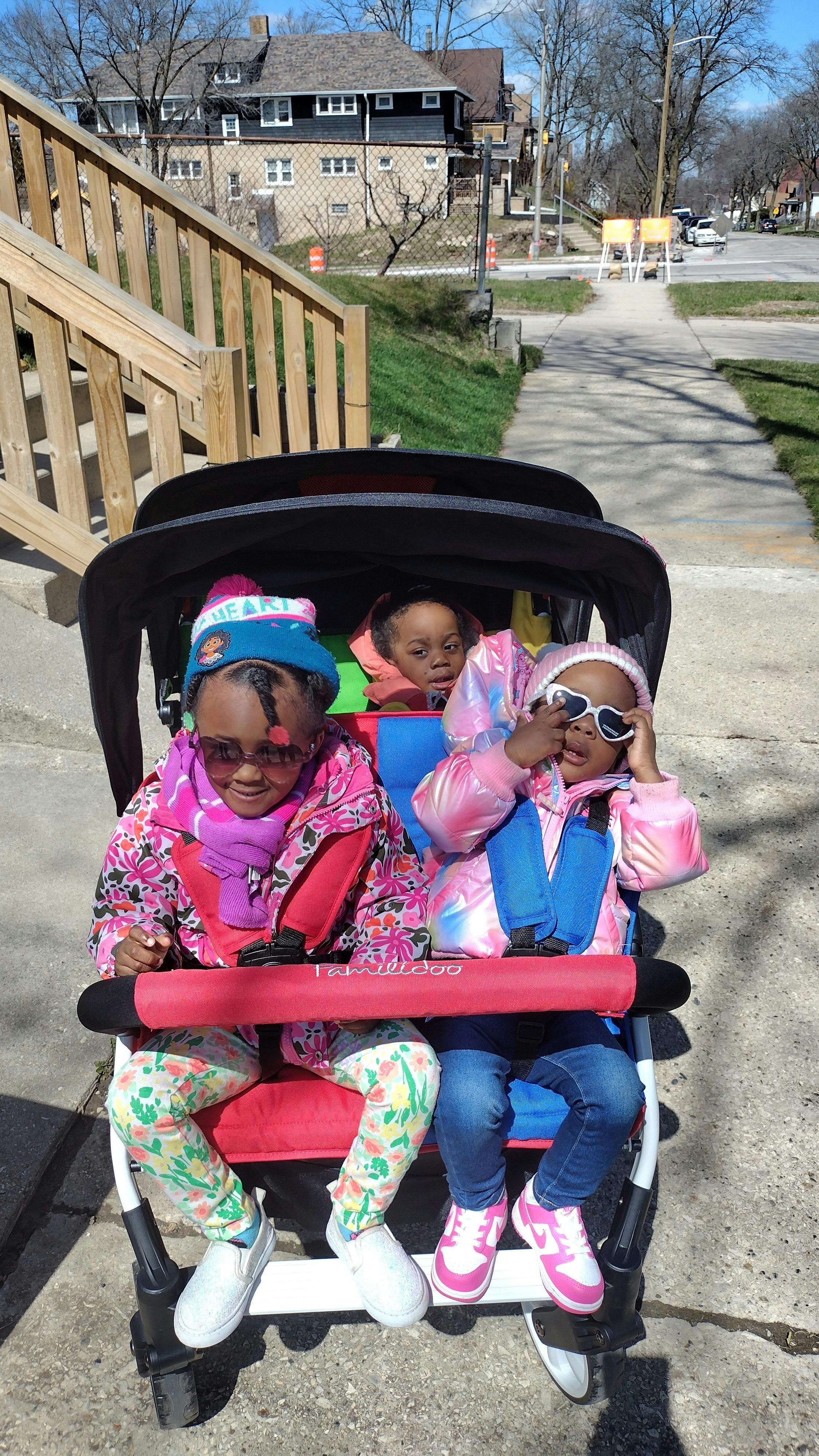 Three children in a stroller on a sidewalk