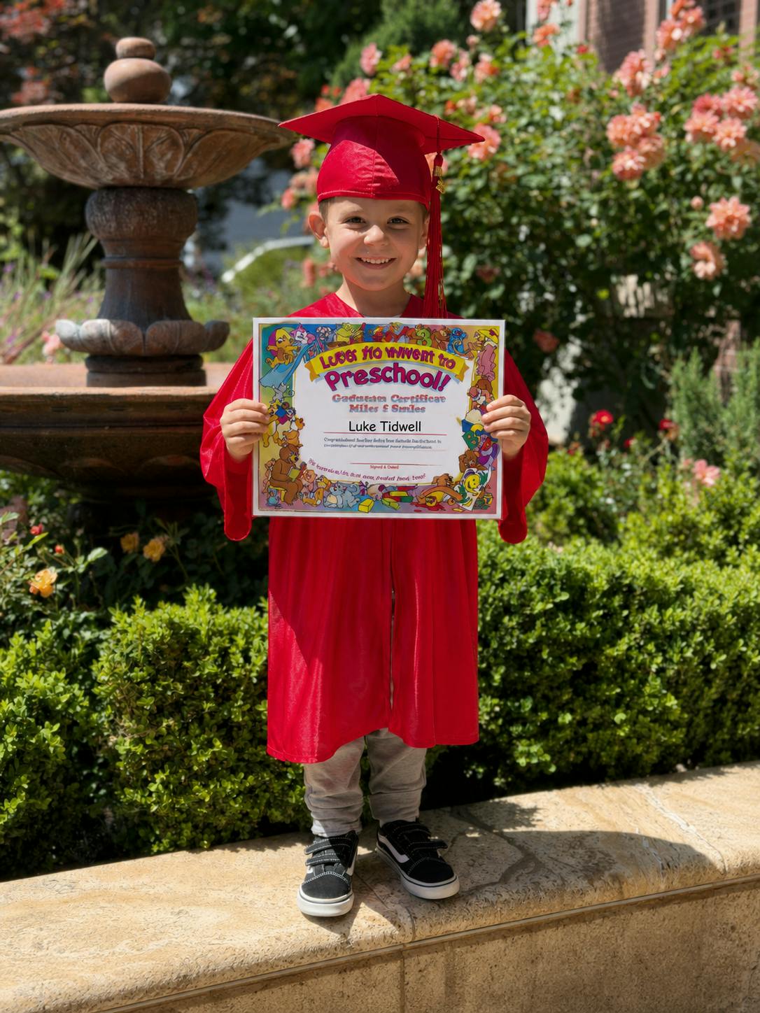 Child in red graduation cap and gown holding a preschool certificate