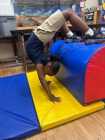 Child doing a backbend over a blue and red gymnastics mat, hands on yellow mat