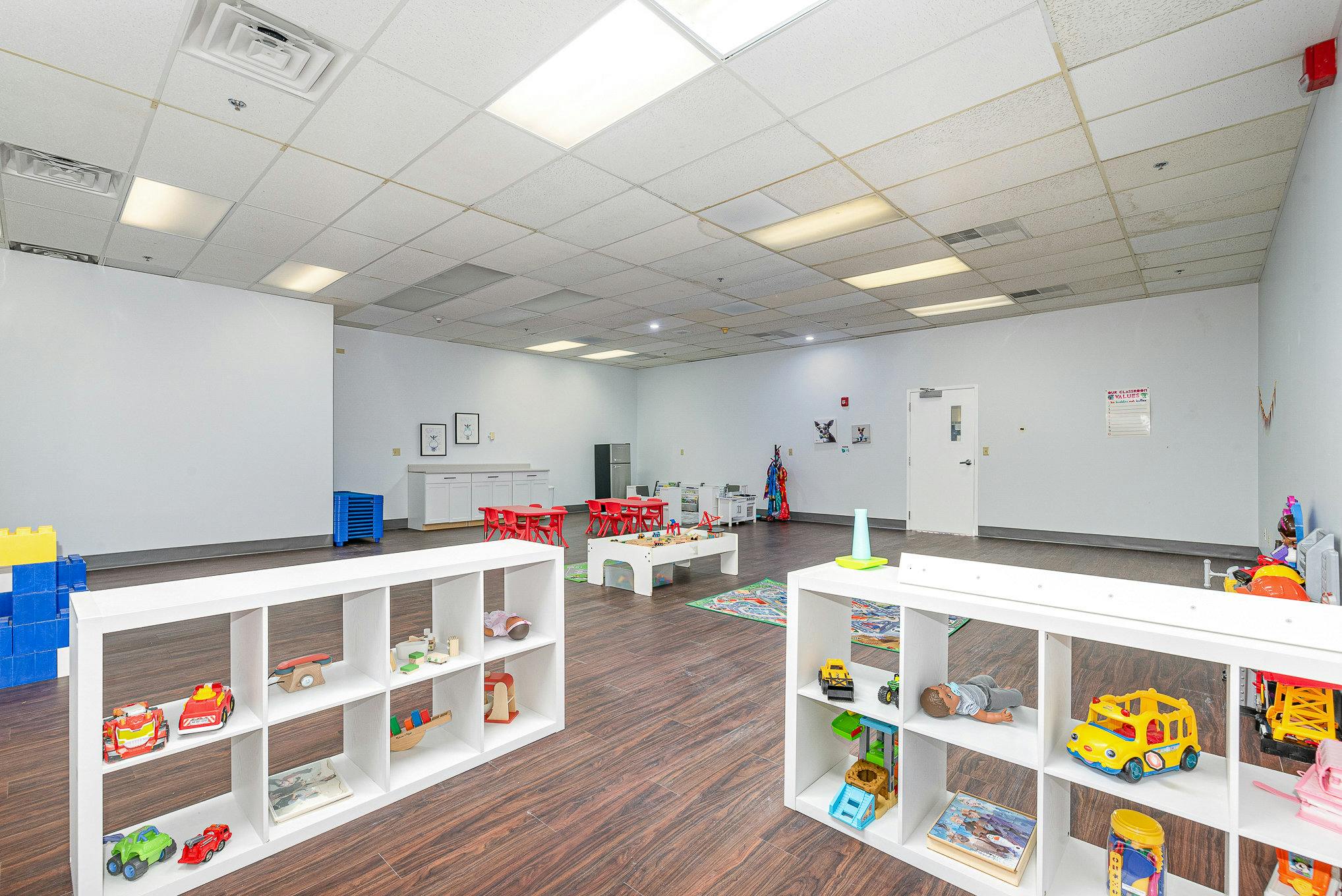 Playroom with white shelves displaying toys and small tables with red chairs