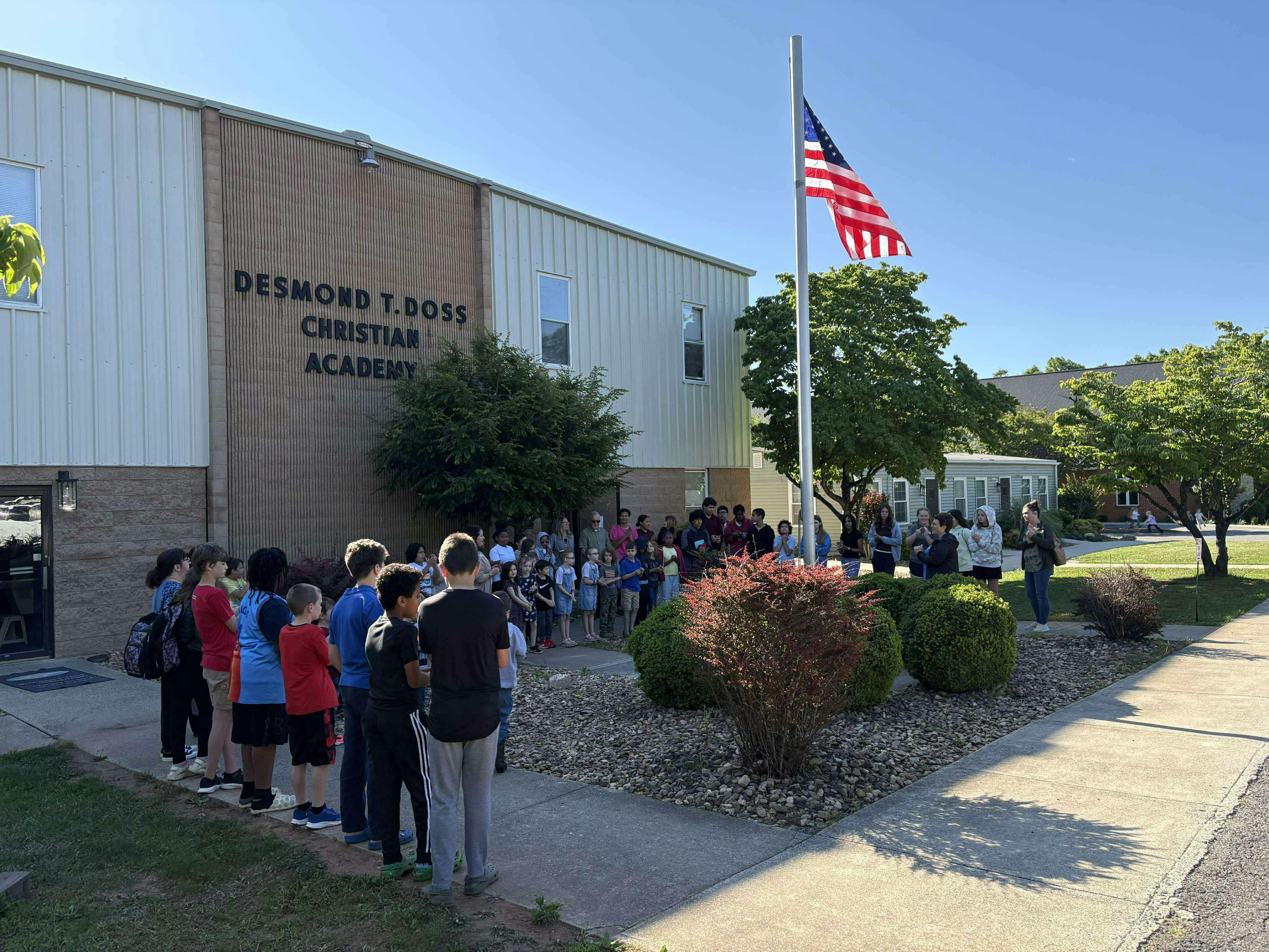 People gathered outside a building with a flag pole and American flag