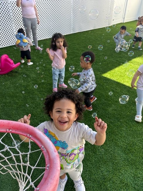 Group of children playing with bubbles on an outdoor artificial grass lawn