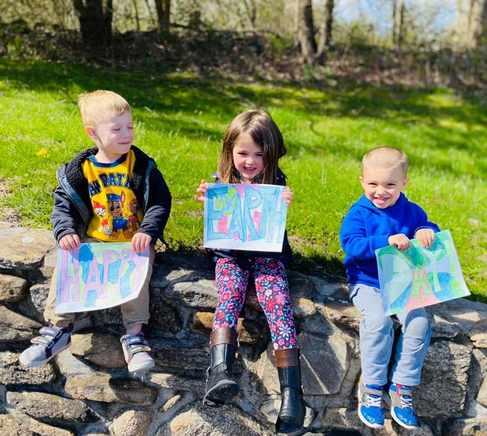 Three children sitting on a stone wall holding up their drawings