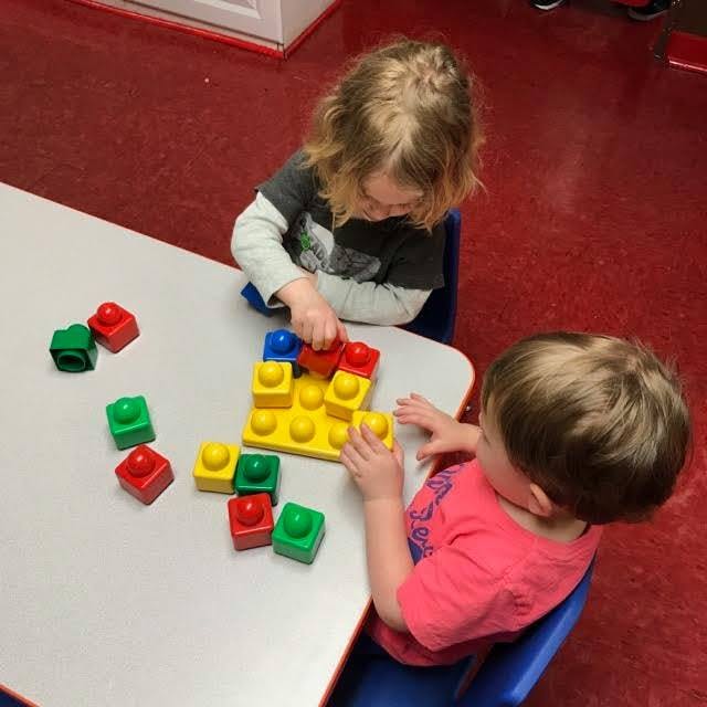 Two children playing with colorful building blocks at a table