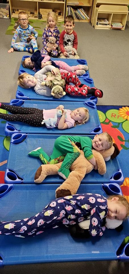 Children in pajamas with stuffed animals on cots