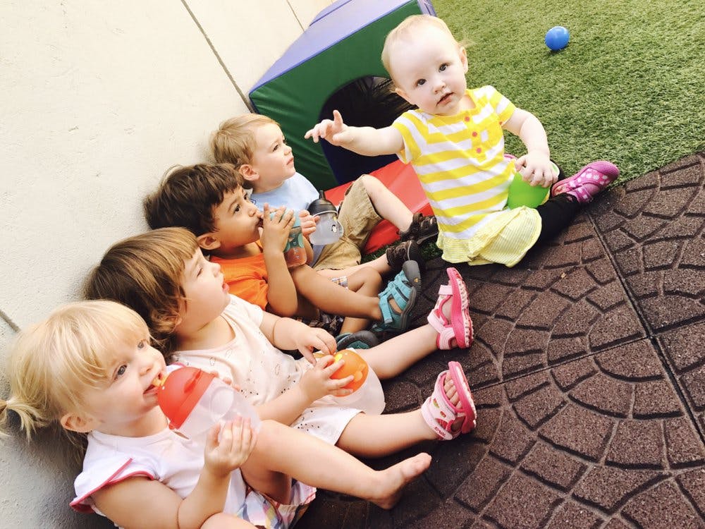 Five children sitting on the ground, one child pointing