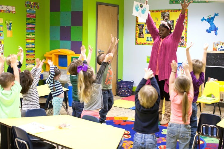 Adult and children with arms raised in a classroom