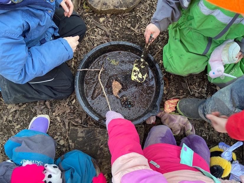 Children playing with mud and sticks in a black tub