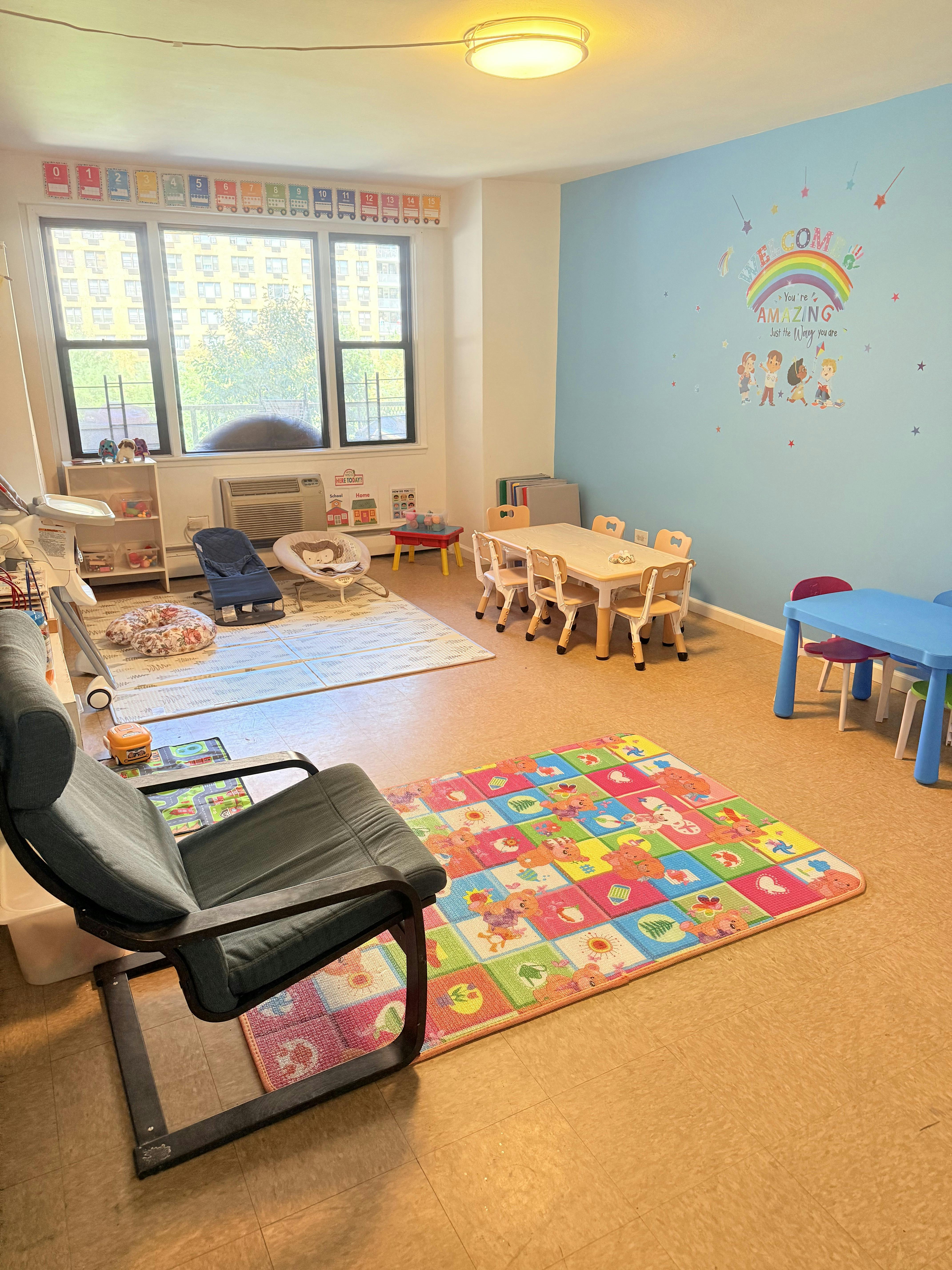 Playroom with small tables and chairs, colorful rug, and blue wall with rainbow decal