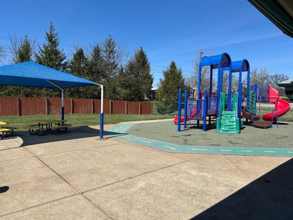 Empty playground with a blue shade structure, picnic tables, and play equipment