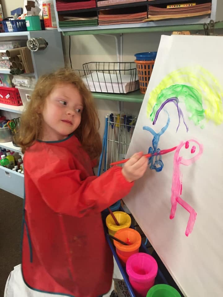 Child in a red smock painting on an easel