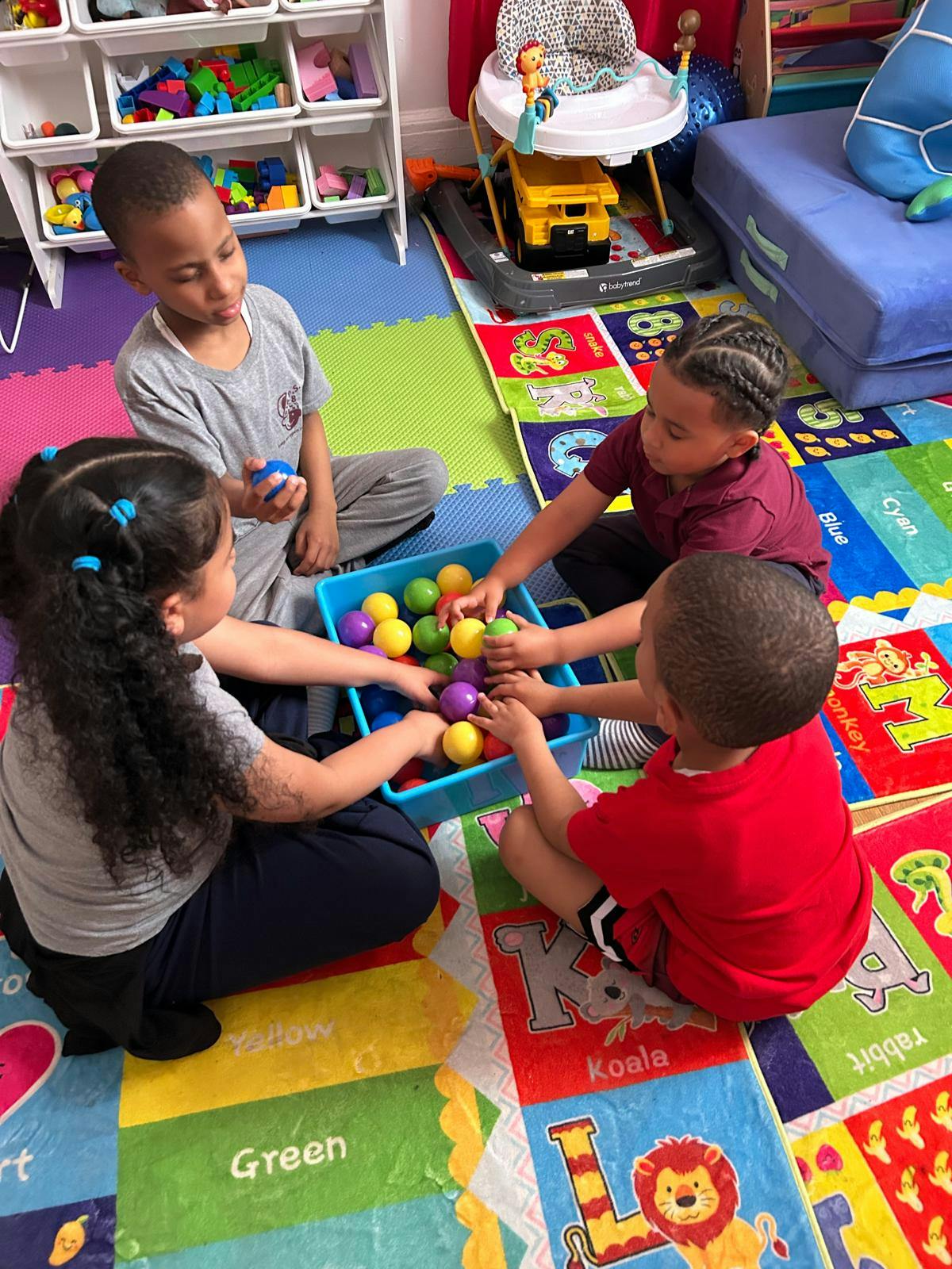 Four children playing with colorful balls in a blue bin on a rug