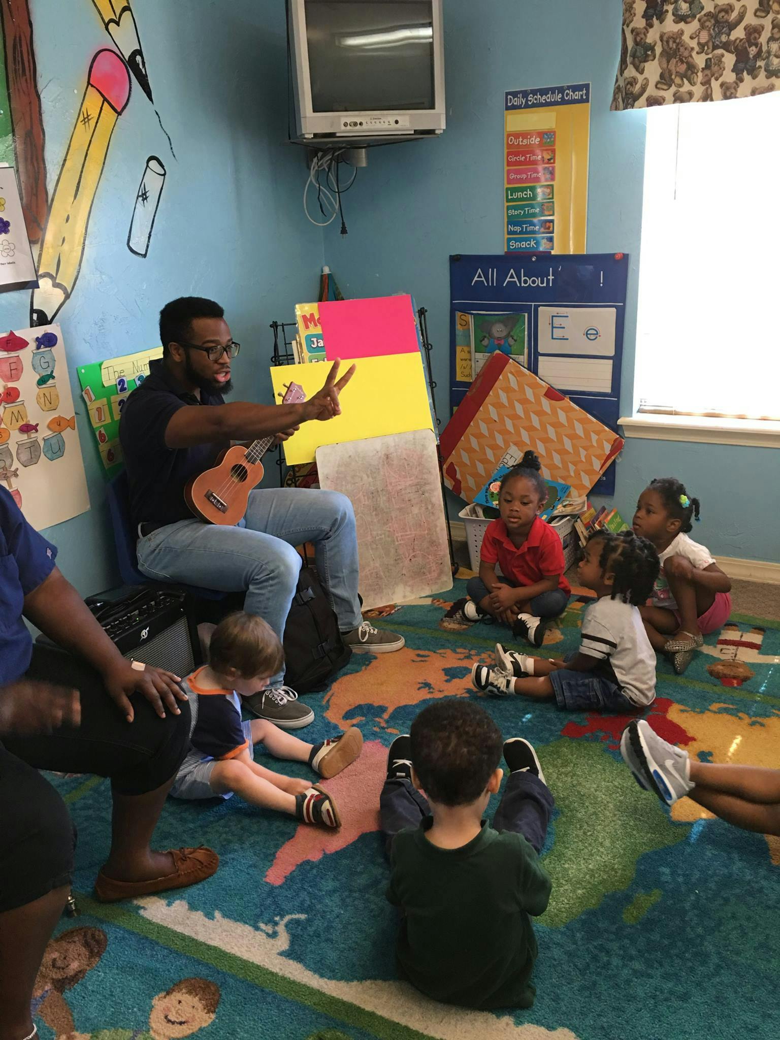 Person playing a ukulele for a group of children sitting on a rug