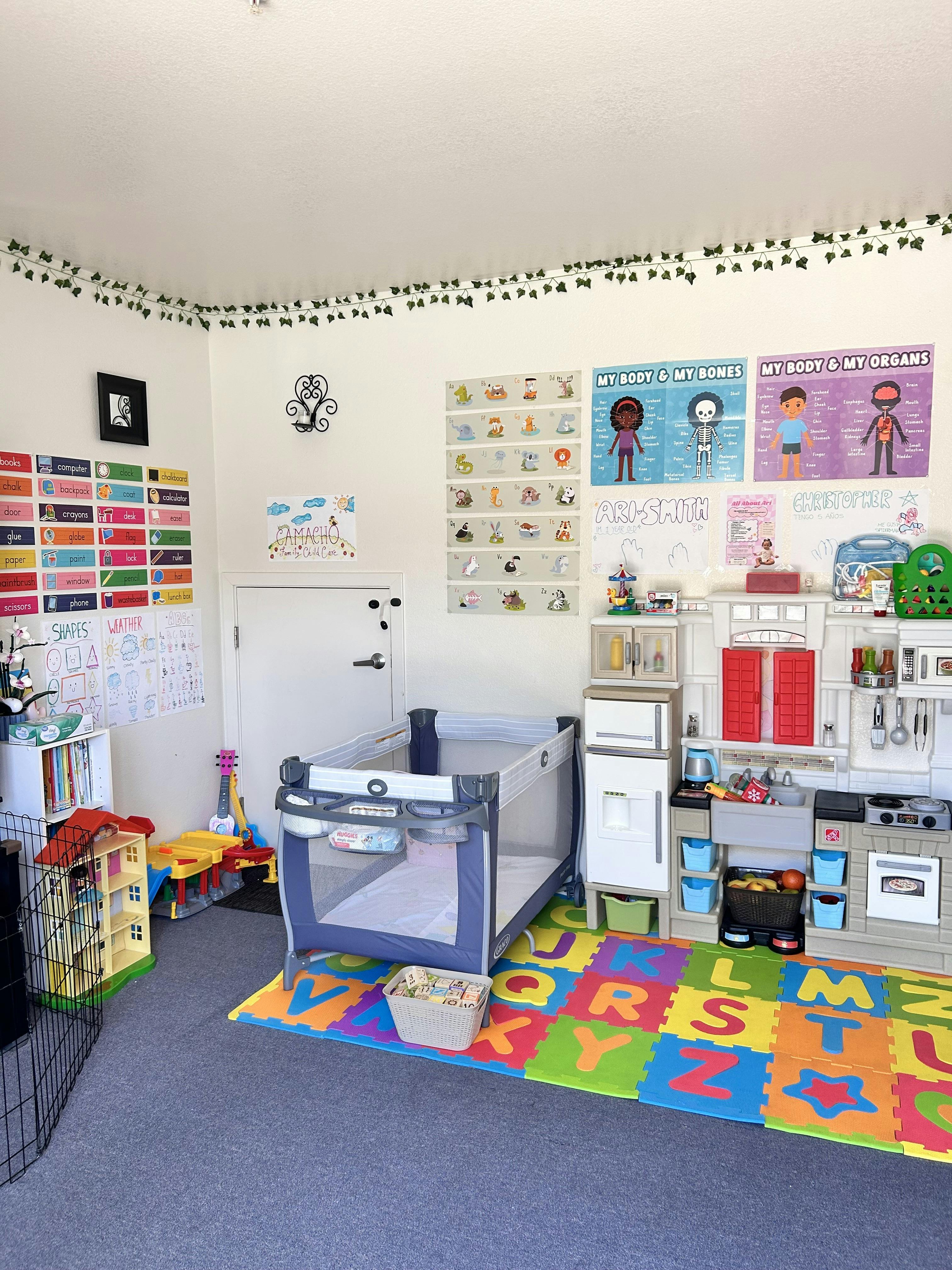 Childcare room with play kitchen, portable crib, and educational posters on the wall