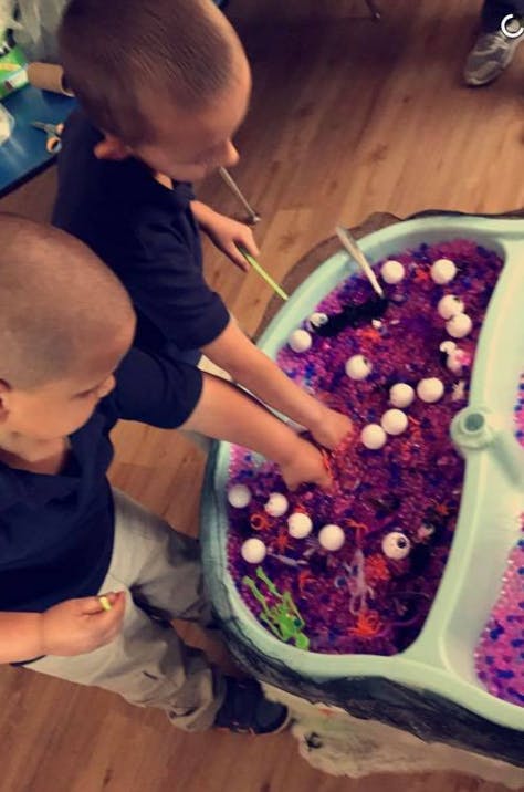 Two children playing with a sensory bin filled with purple material and orange materials