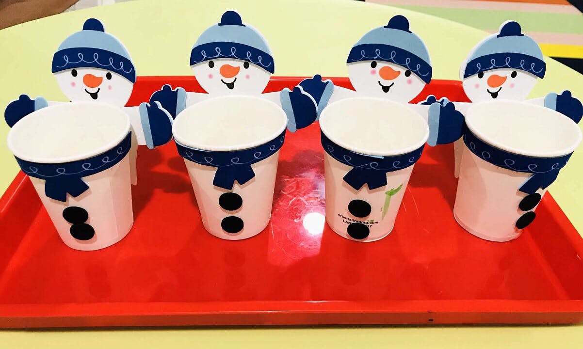 Four snowman-themed paper cups on a red tray
