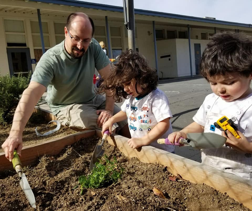 Person and two children planting in a garden bed