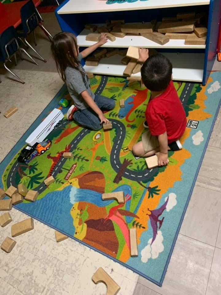 Two children playing with wooden blocks on a colorful rug
