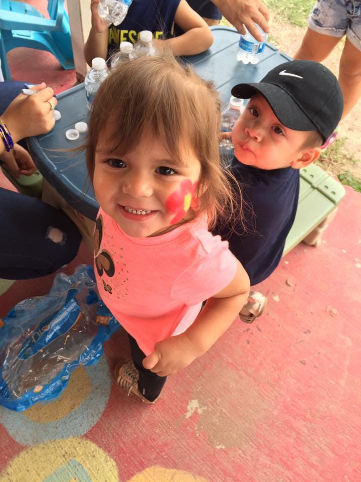 Child with face paint smiling, another child in a cap behind