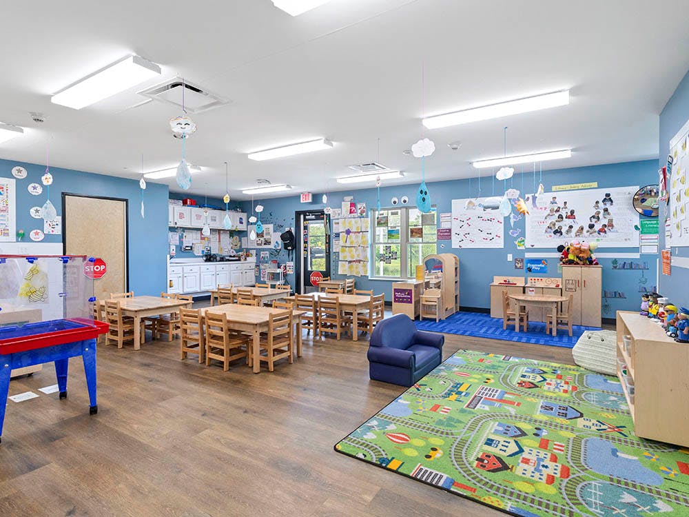 Classroom with small wooden tables and chairs, play rug, and activity areas