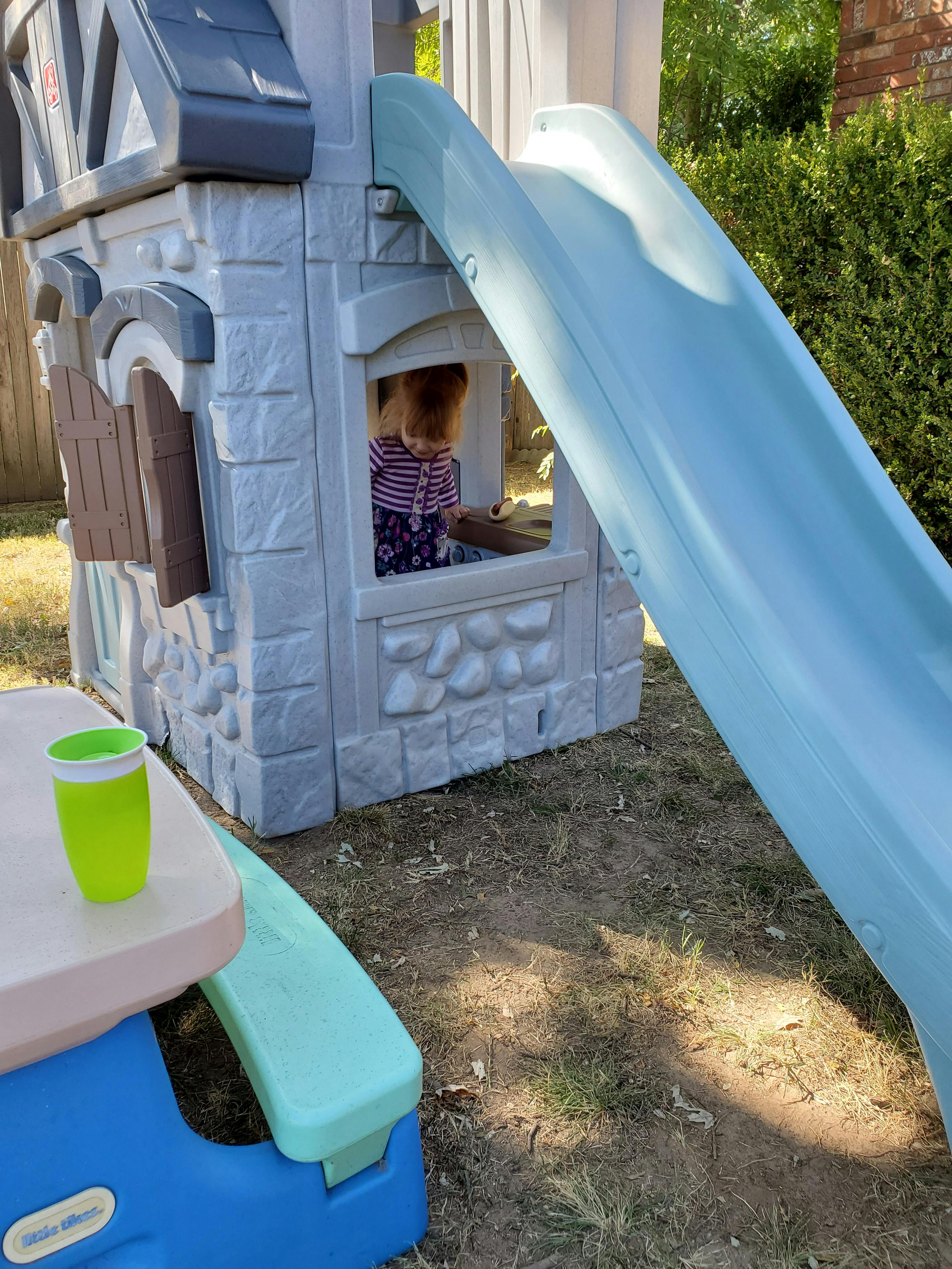 Child looking out a window of a playhouse with a slide