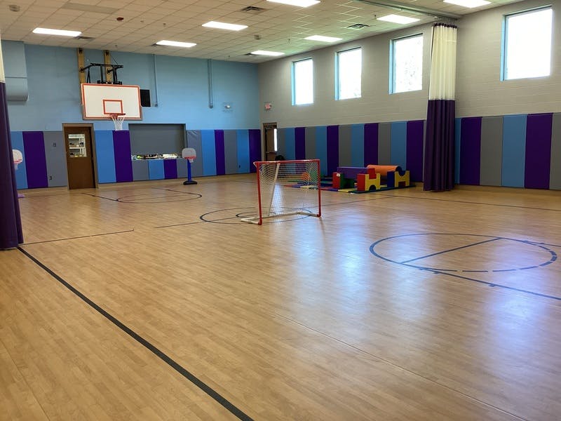 Empty gymnasium with a basketball hoop, small hockey net, and soft play equipment