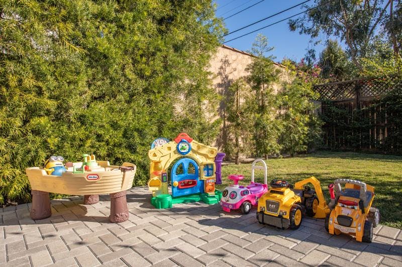 Children's outdoor toys including a playhouse, sand table, and ride-on vehicles