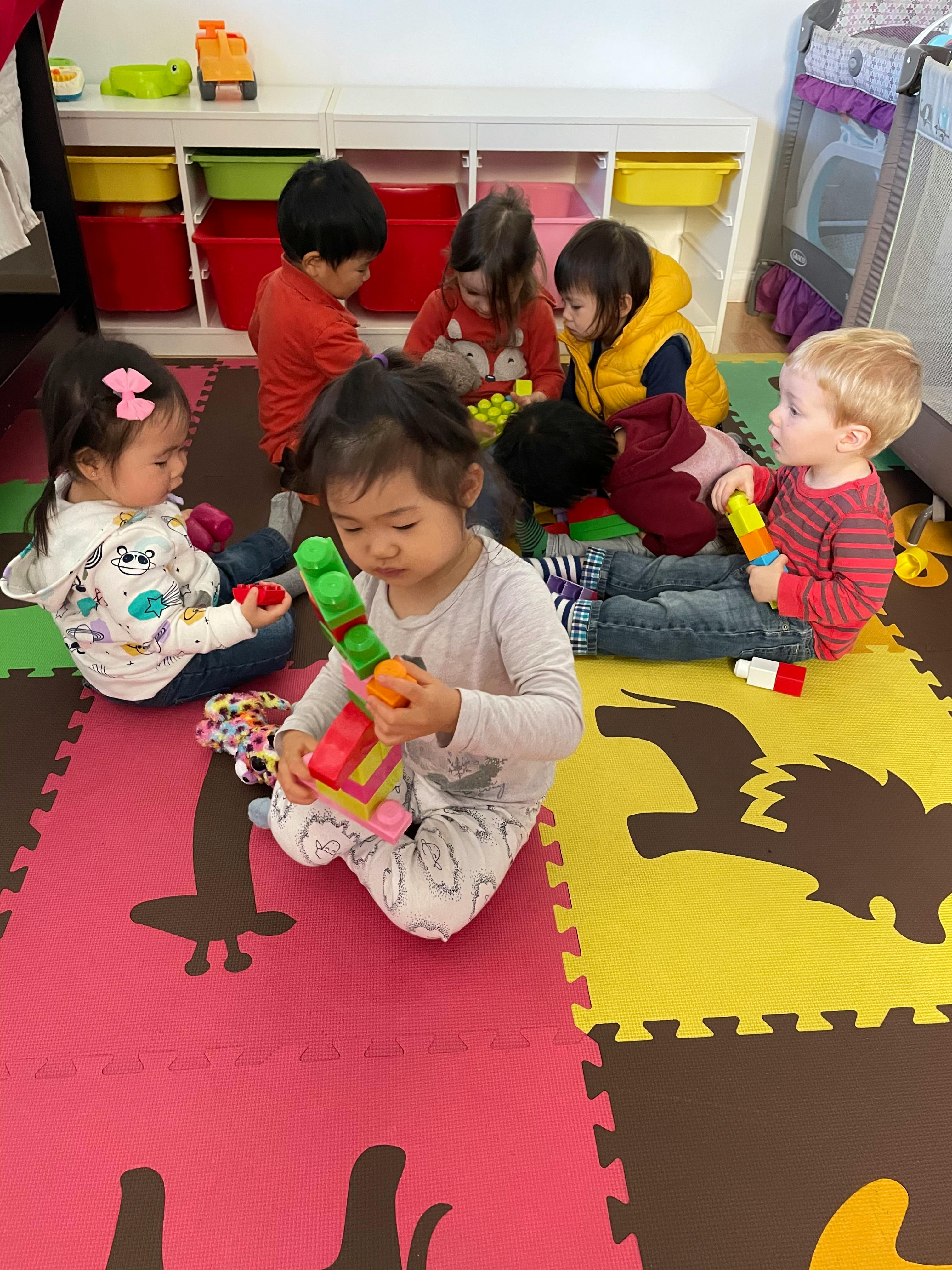 Multiple children playing with toys on a colorful mat