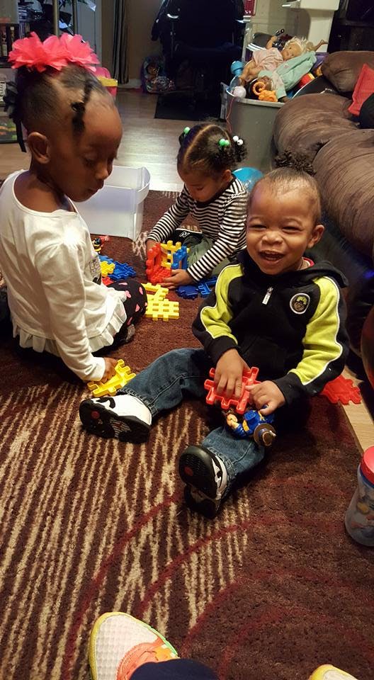 Three children playing with colorful building blocks on a rug