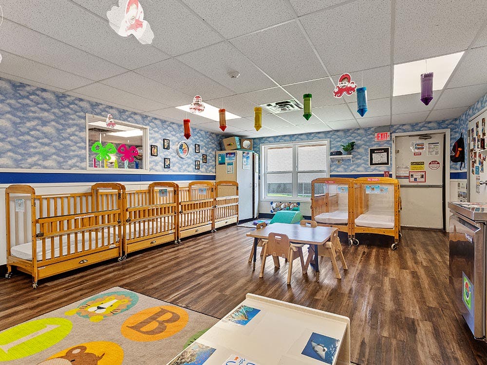 A colorful room with multiple cribs, a child-sized table, and bright decorations