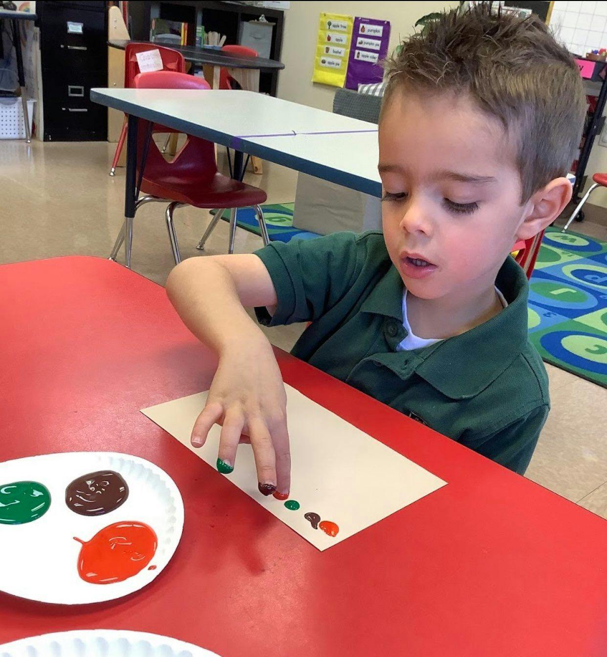 Child finger painting on paper at a red table in a classroom