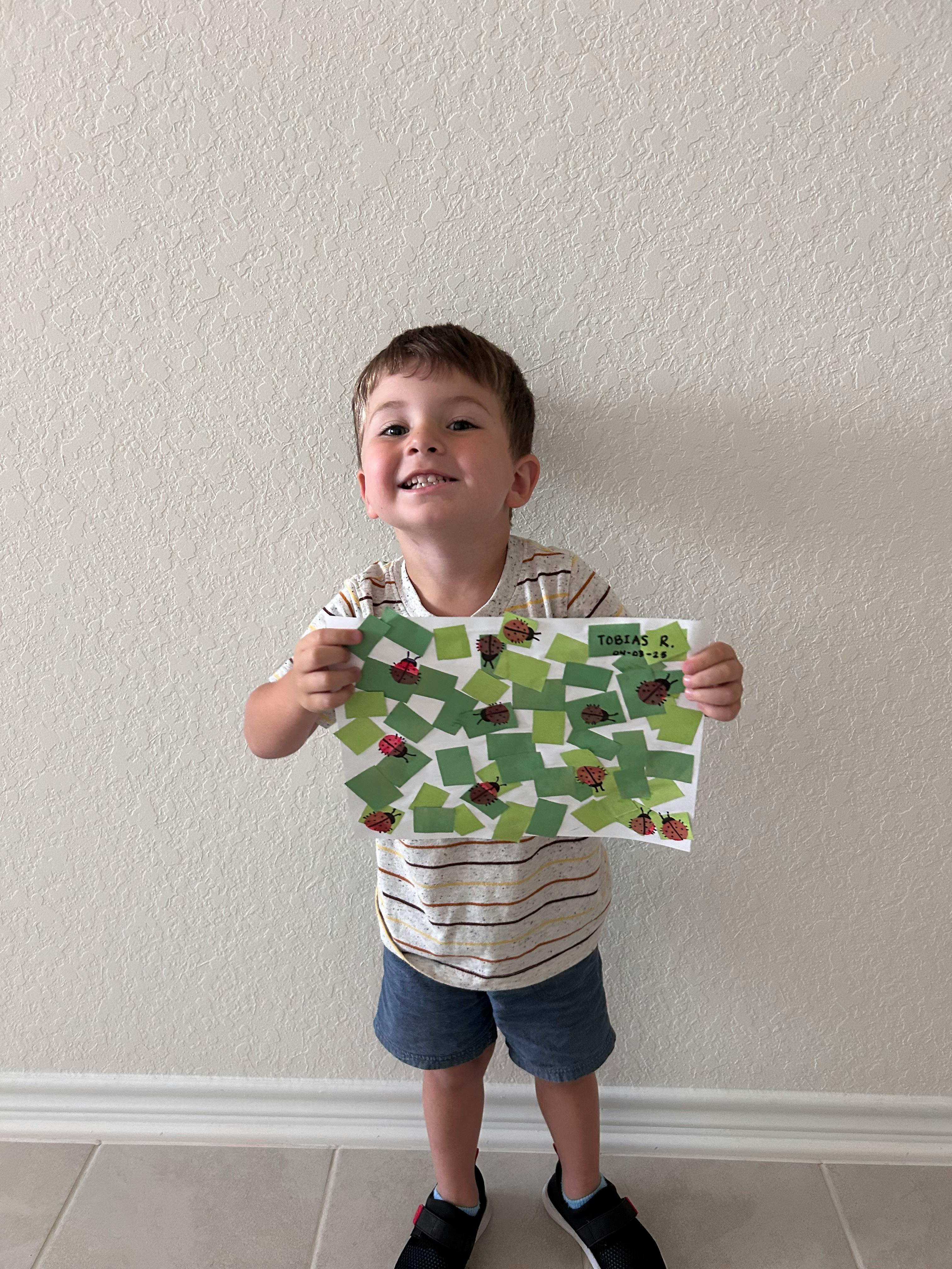 Child holding up a paper with green squares and ladybugs
